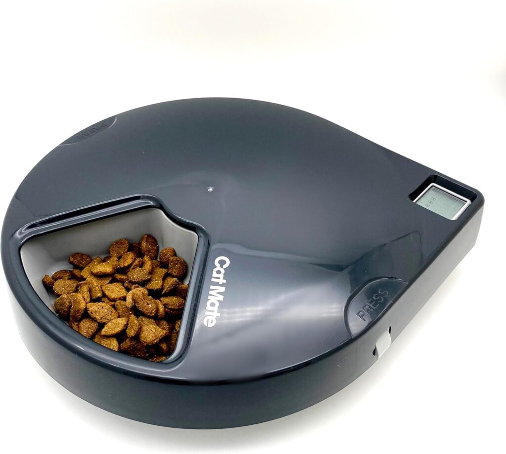 A round, black automatic pet feeder labeled Cat Mate, partially filled with dry cat food, features a small display screen and a PRESS button on the right side—an ideal gift idea for any cat owner. alwaysagift.co.uk