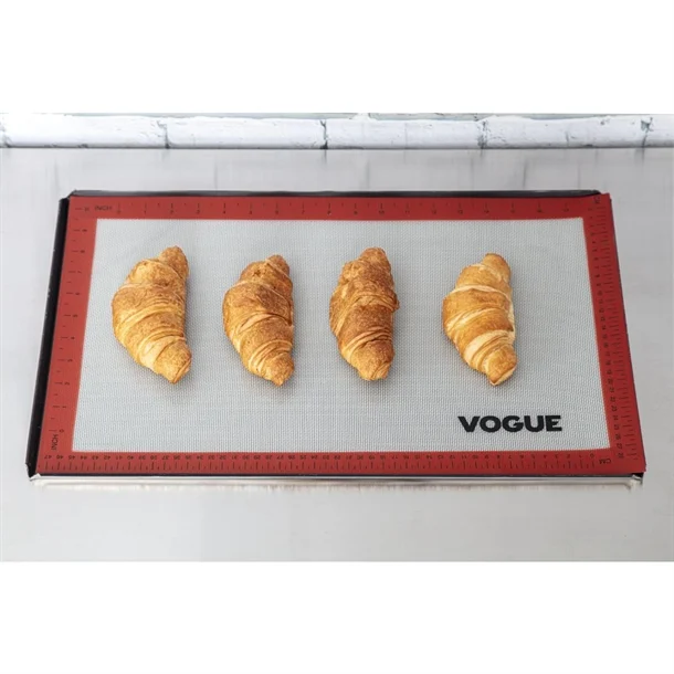 Four croissants are evenly spaced on a non-stick red and gray baking mat labeled VOGUE, placed on a metal baking tray against a white countertop—an ideal choice for gifts for bakers or thoughtful baking gifts. gift idea