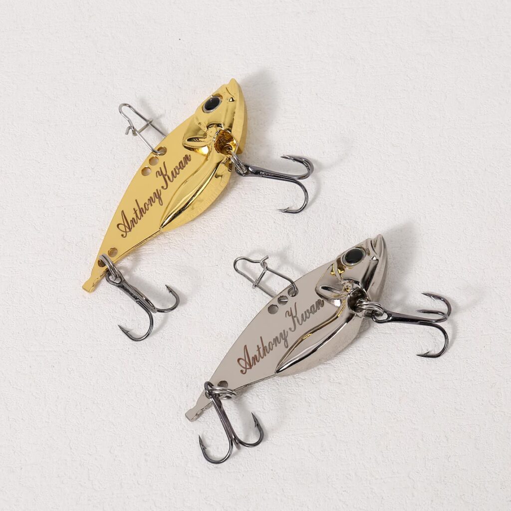 Two metallic fishing lures, one gold and one silver, each with two treble hooks and engraved with the name Anthony Kwan, displayed on a white textured surface—a thoughtful gift idea for any angler. alwaysagift.co.uk