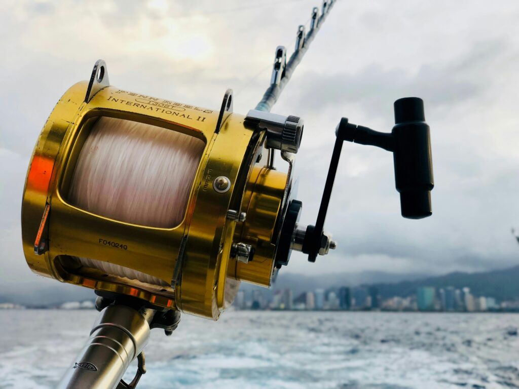 A close-up of a gold fishing reel attached to a rod on a boat, with the ocean and a distant city skyline under cloudy skies in the background—perfect inspiration for unique fishing gifts or gift ideas for men who love the water. gift idea