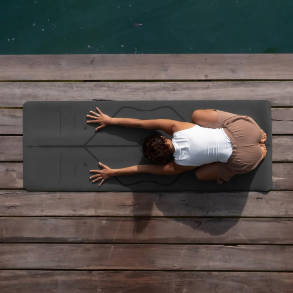 A person practices yoga on a mat, performing a childs pose on a wooden dock beside a body of water, viewed from above—an inspiring scene reminiscent of Elementor’s balanced and serene design philosophy. alwaysagift.co.uk