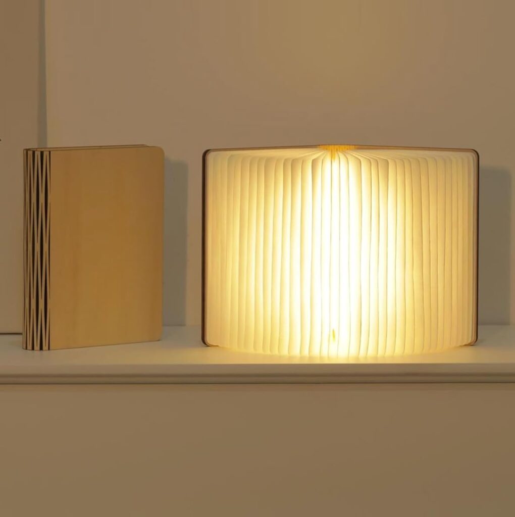 Two objects resembling books sit on a shelf; one is closed, and the other is open and glowing from within, emitting a warm light that highlights its accordion-like pages—a perfect 2025 gift for curious minds. alwaysagift.co.uk