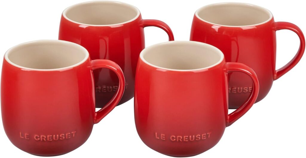 Four red ceramic mugs with Le Creuset embossed near the base, arranged in a staggered formation. The mugs have a glossy finish and rounded shape with handles on the right side, perfect for brightening up your Elementor-designed kitchen display. alwaysagift.co.uk