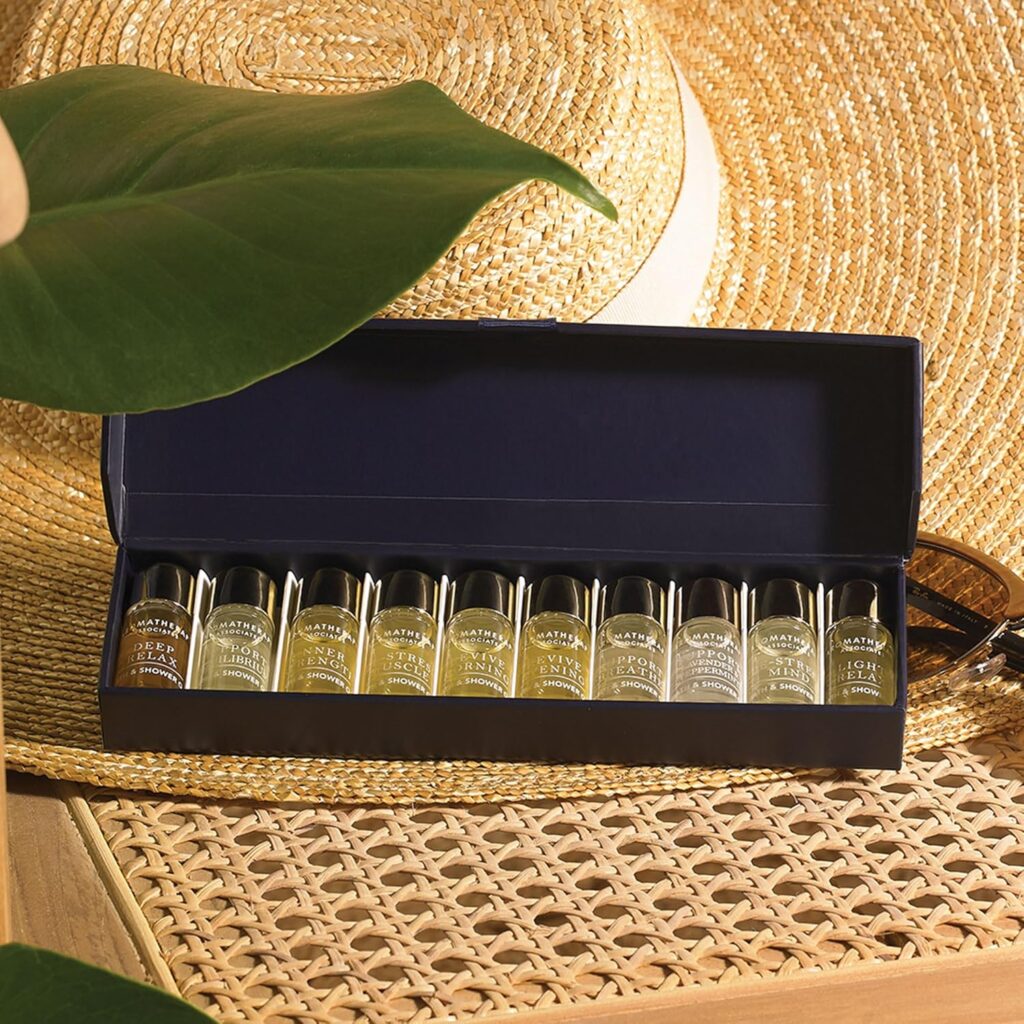 A box of ten small glass perfume vials is displayed open on a woven mat, alongside a large straw hat, sunglasses, green leaves, and an Elementor-designed card in a sunlit setting. alwaysagift.co.uk
